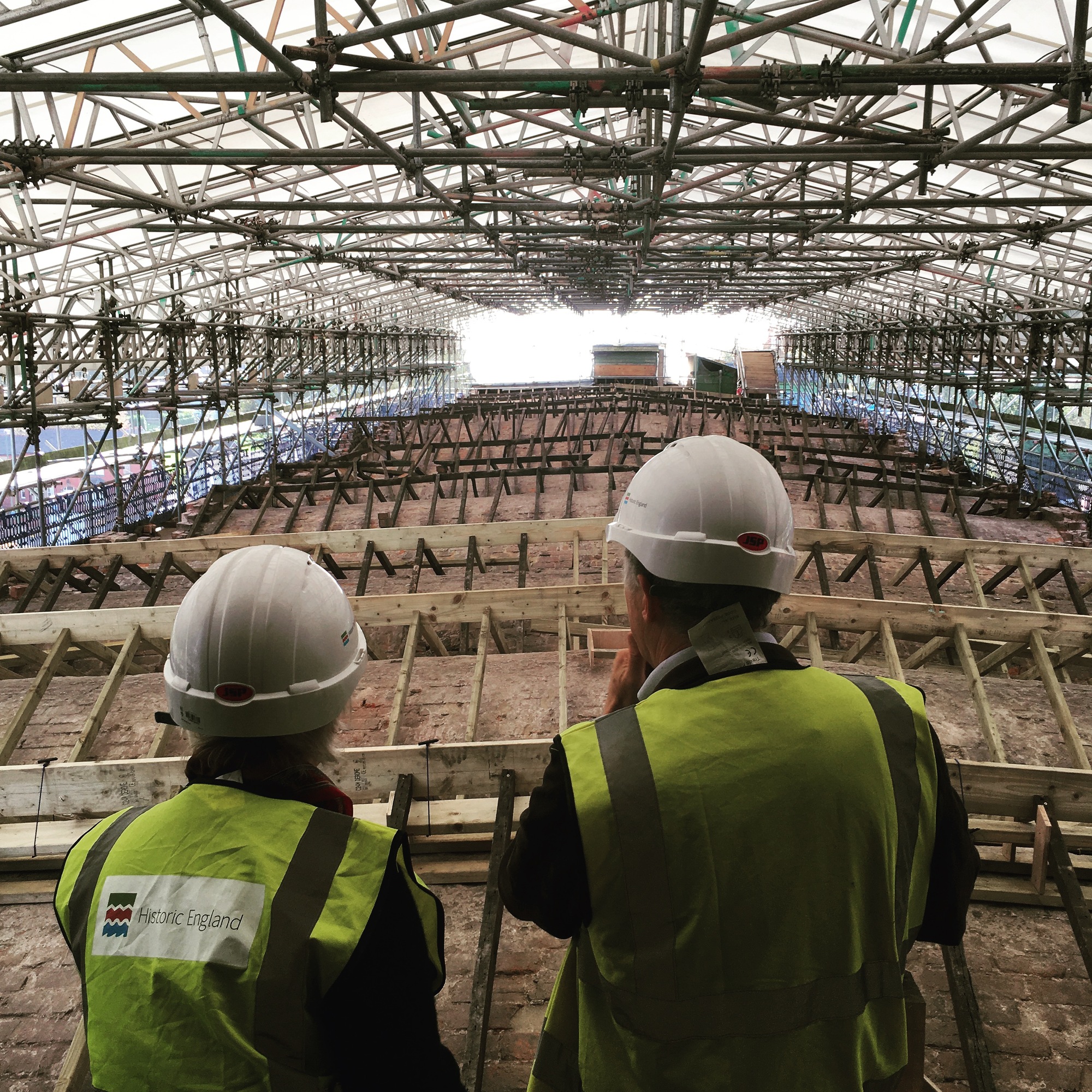 Two people overlooking repairs to an historic factory roof, surrounded by scaffolding.