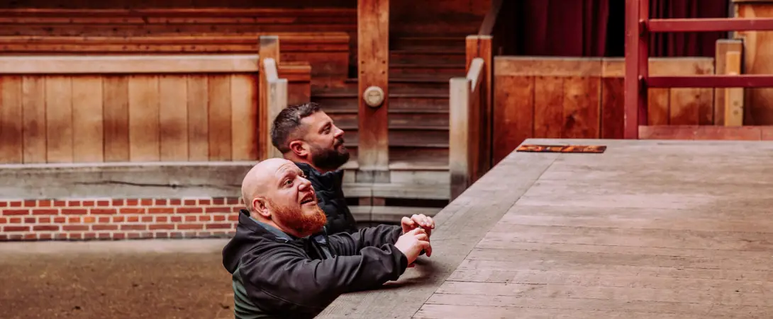 Two men in the Globe Theatre looking up at the stage from the stalls.