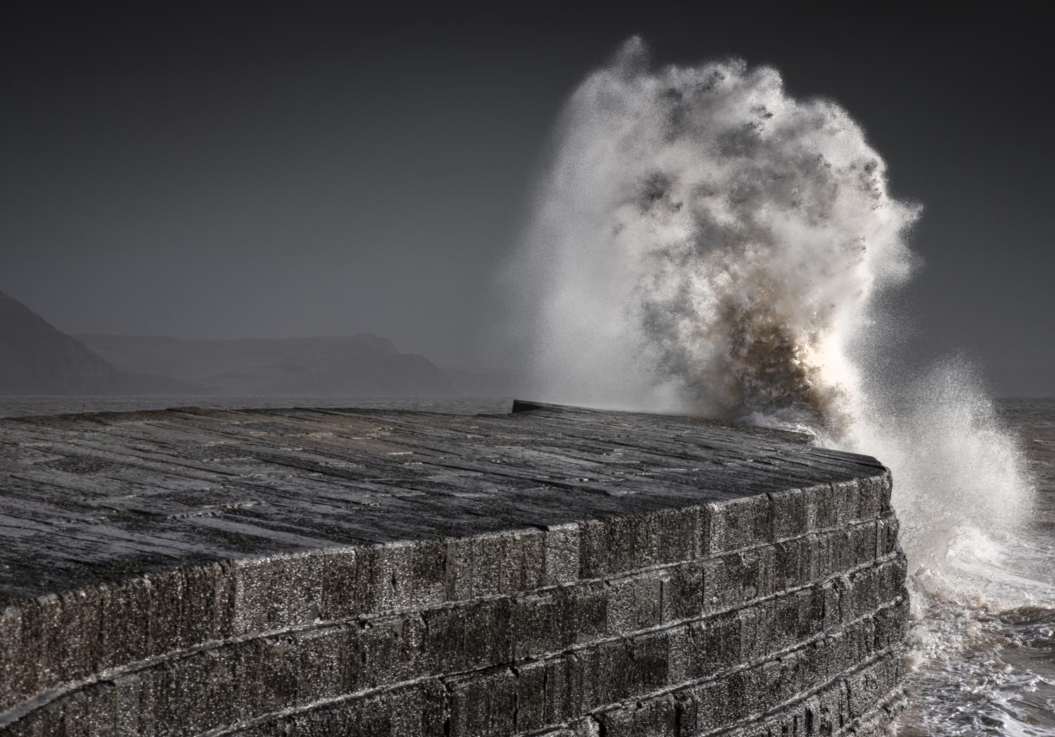 A wave crashing on a harbour wall in a storm.