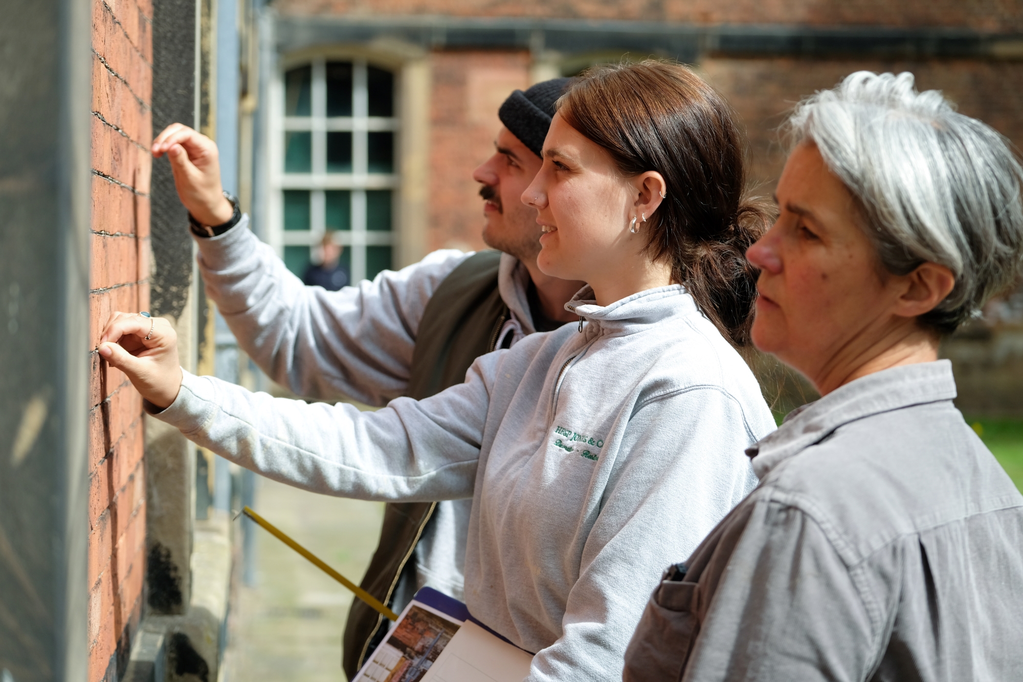 Three people repairing a brick wall.